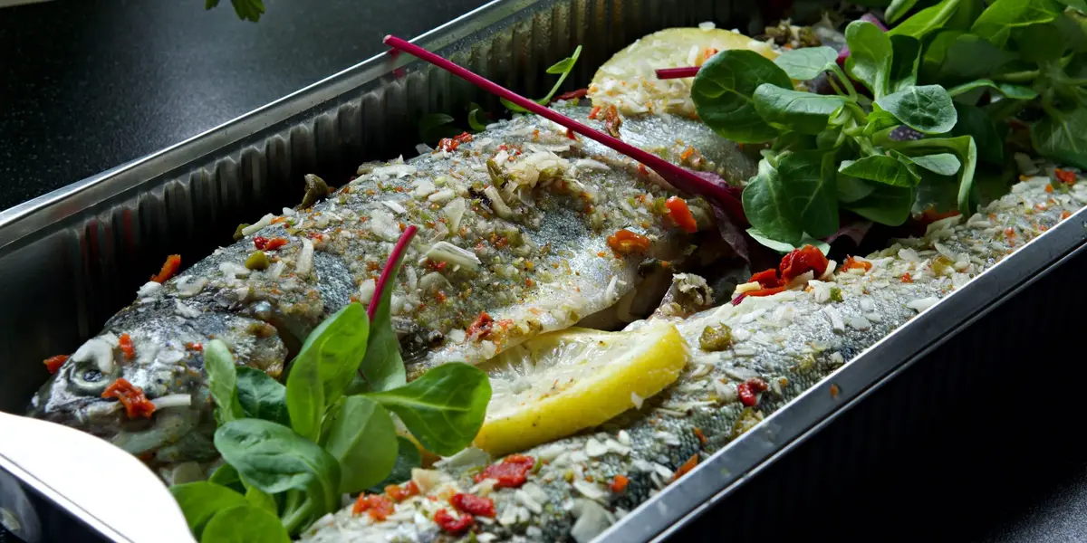 Poisson entier doré au four dans un plat, citrons et herbes fraîches, vue rapprochée